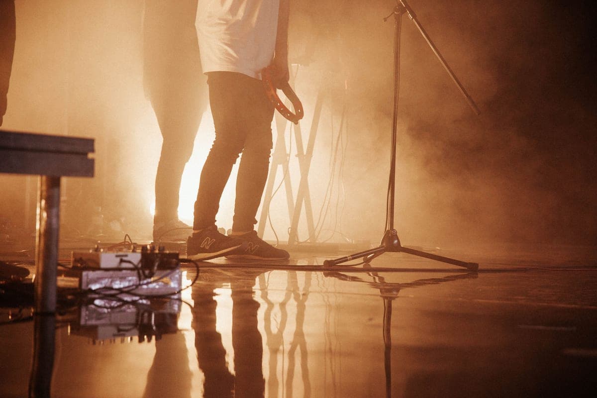 A musician operating a loop pedal on a stage floor